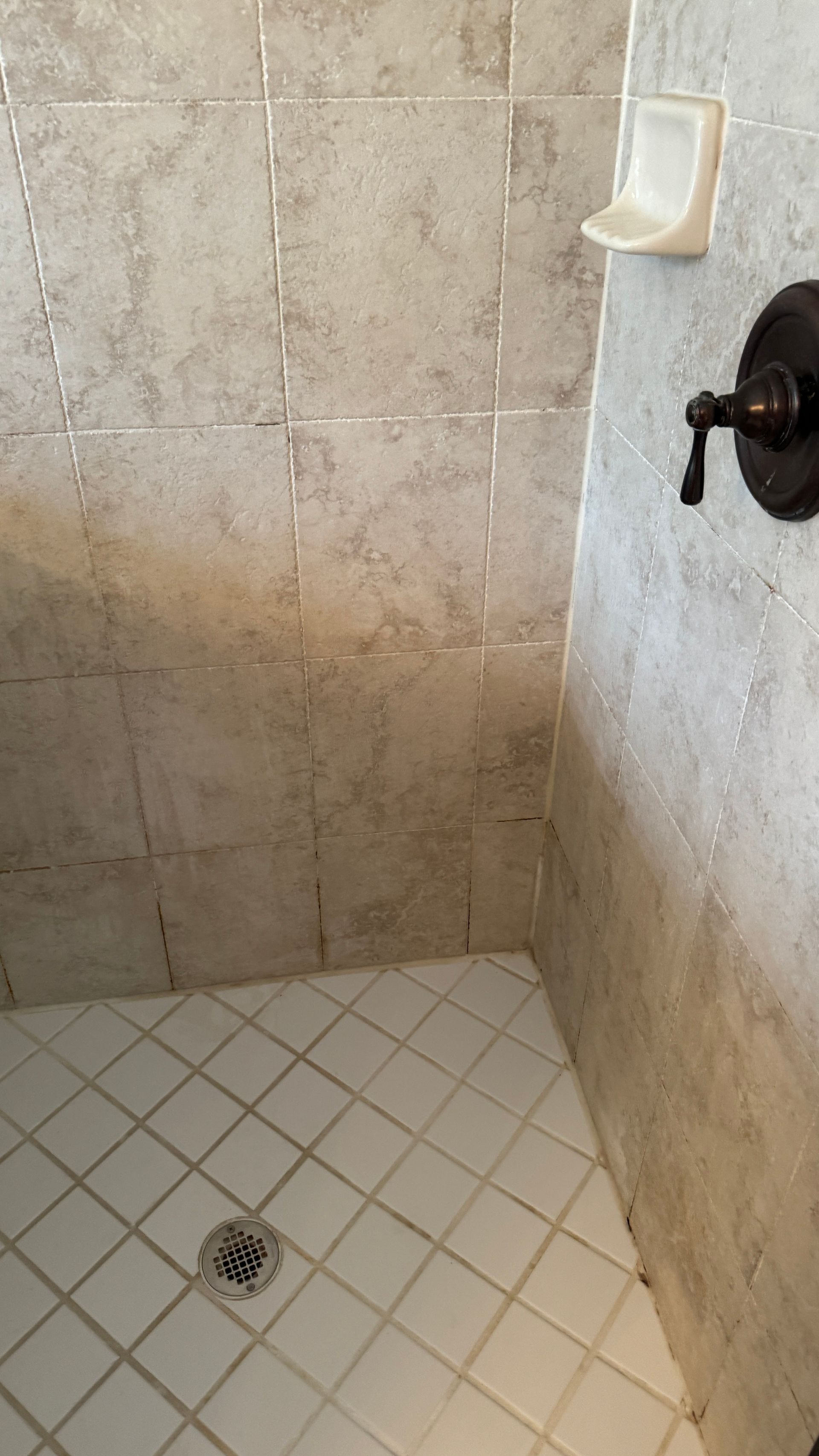 A shower stall with white tiles and a soap dish on the wall.