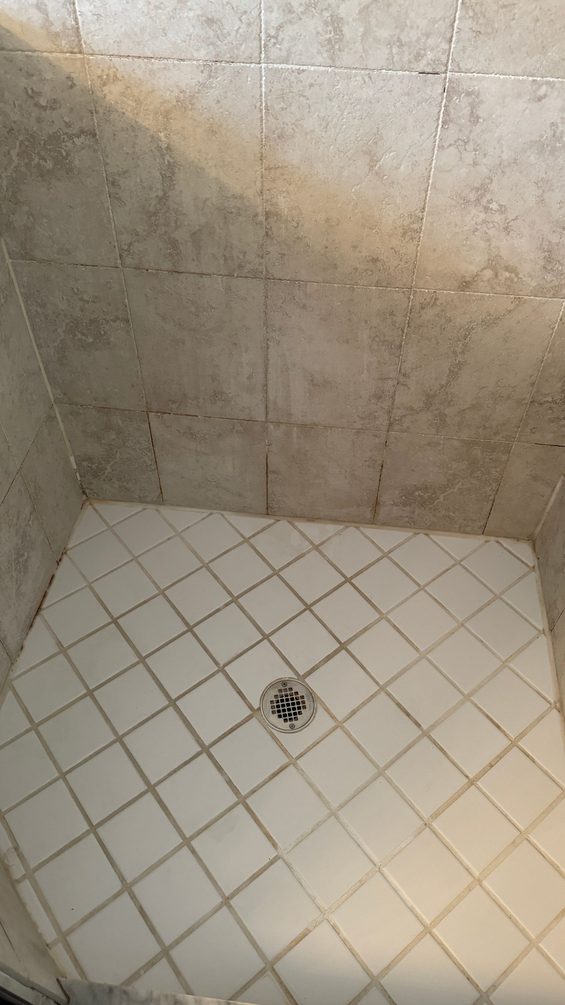 A shower stall with white tiles and a drain.