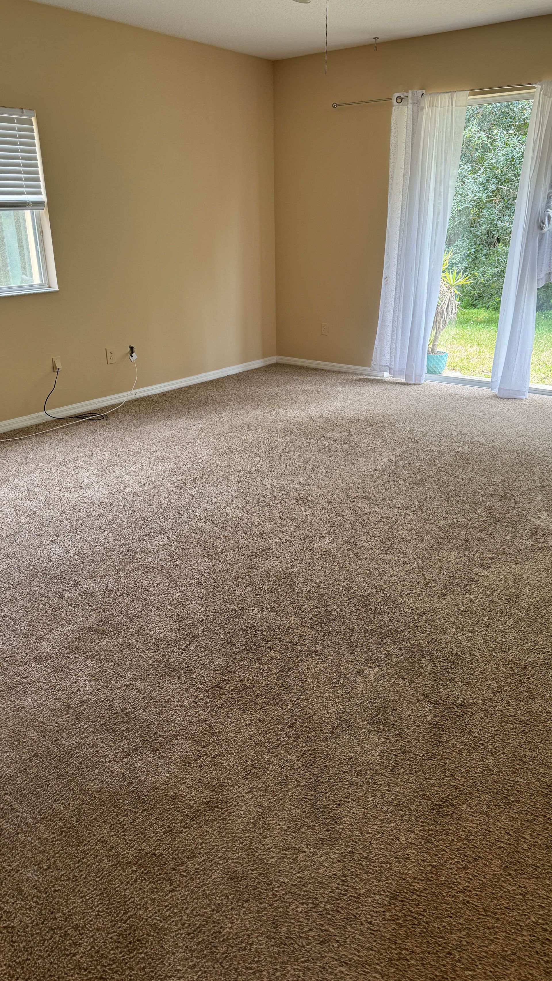 An empty living room with a sliding glass door and a window.