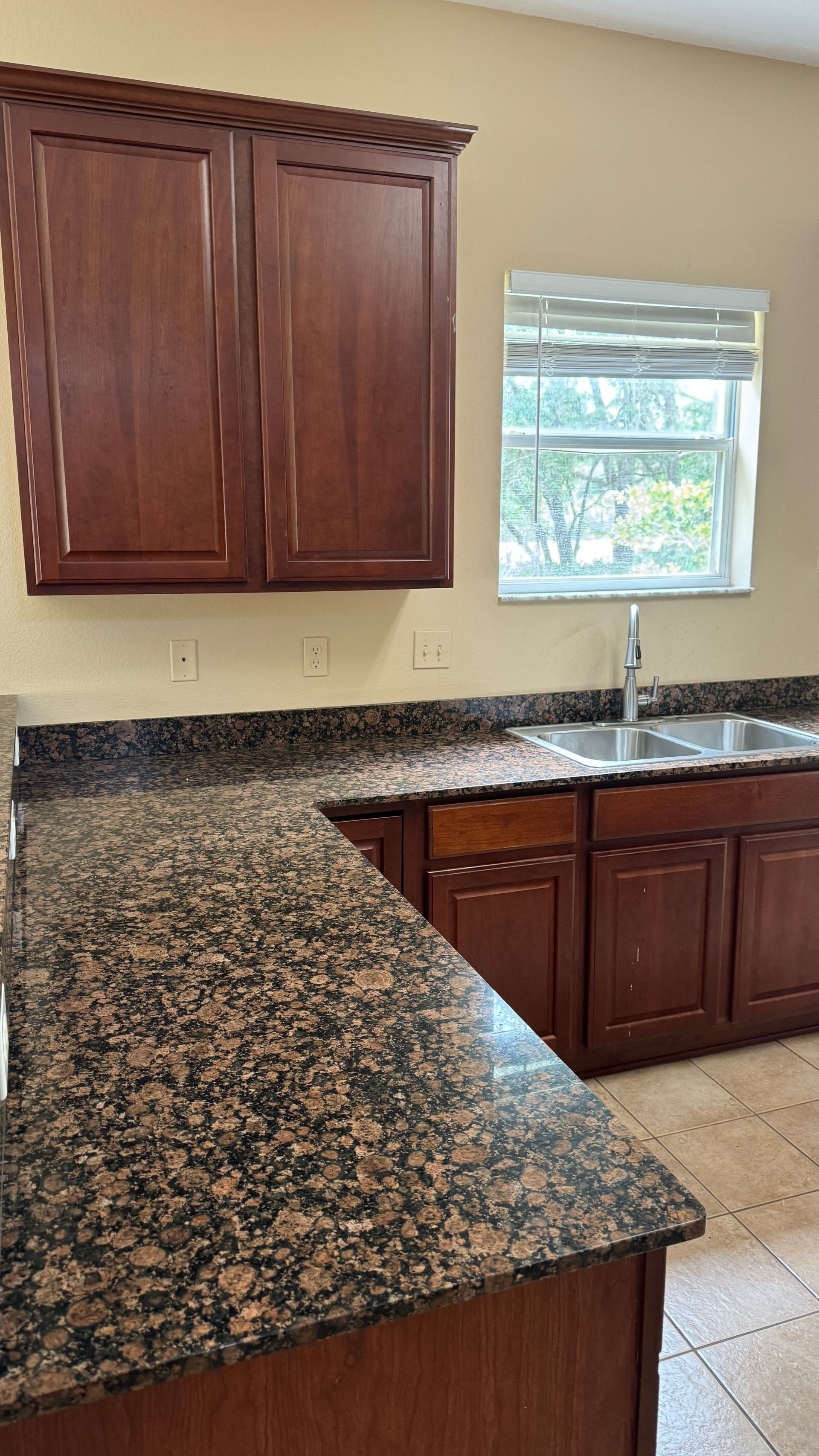 A kitchen with granite counter tops , wooden cabinets , a sink and a window.