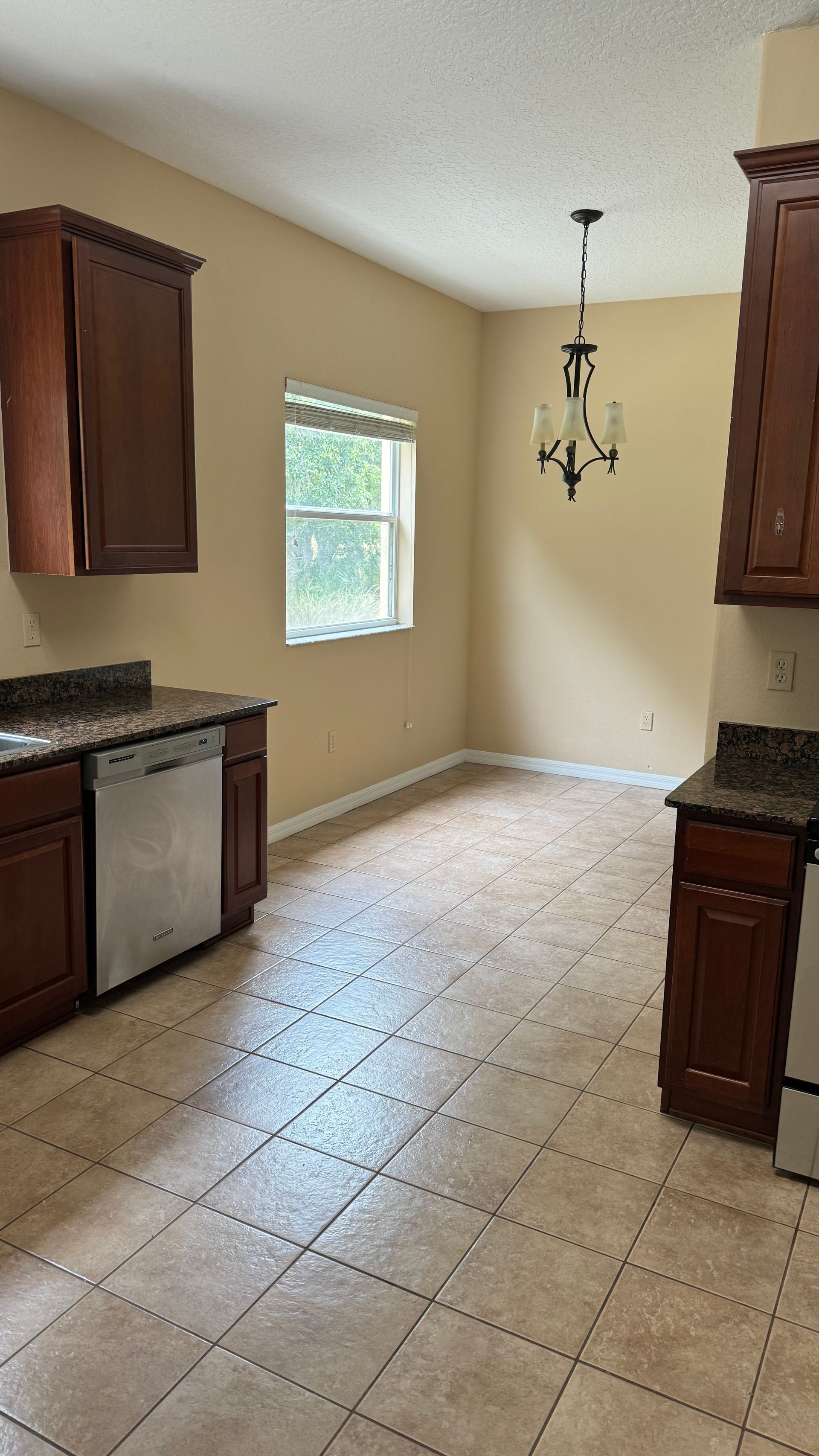 An empty kitchen with wooden cabinets and a stainless steel dishwasher.