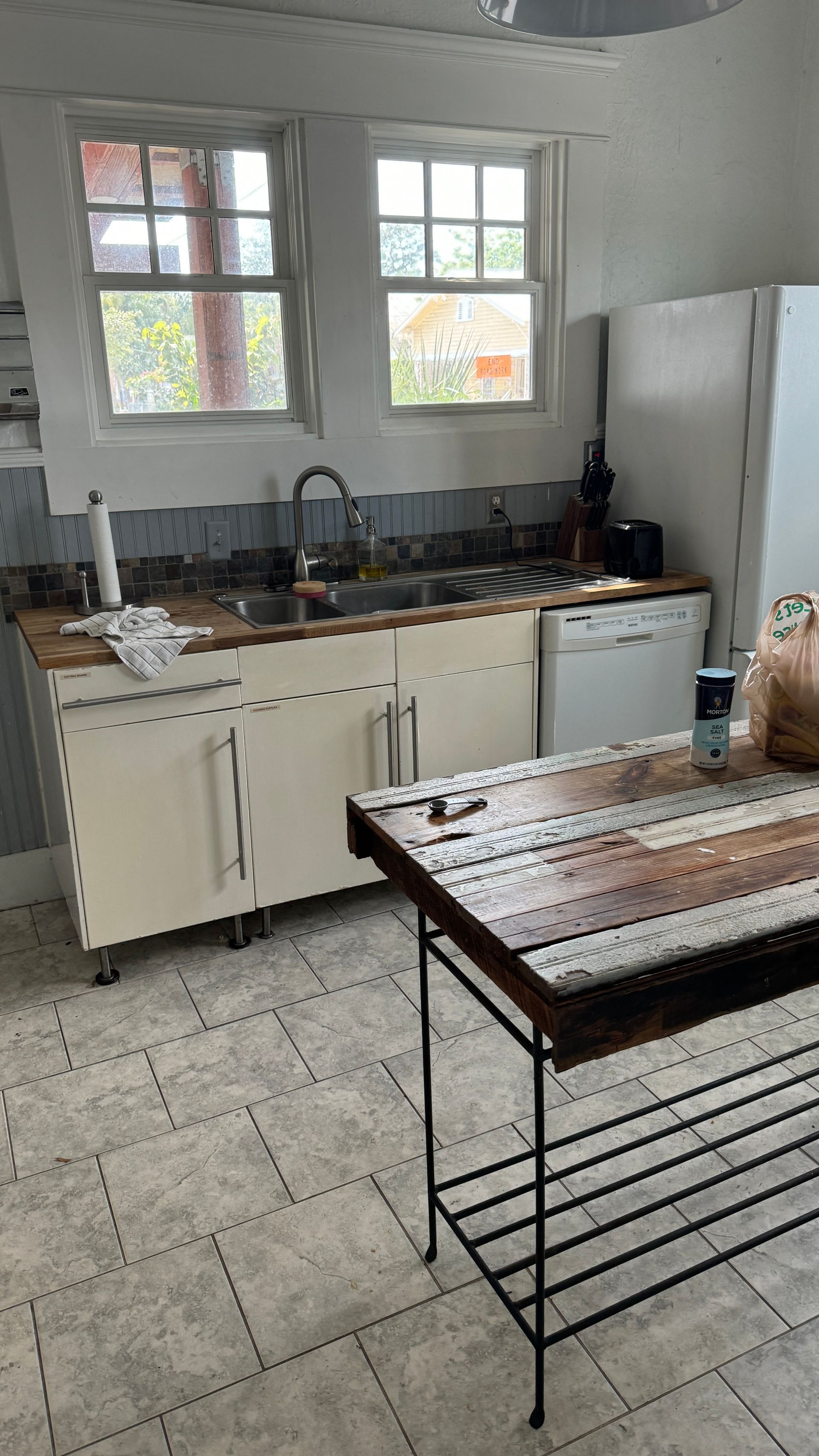 A kitchen with a wooden table , sink , dishwasher and refrigerator.