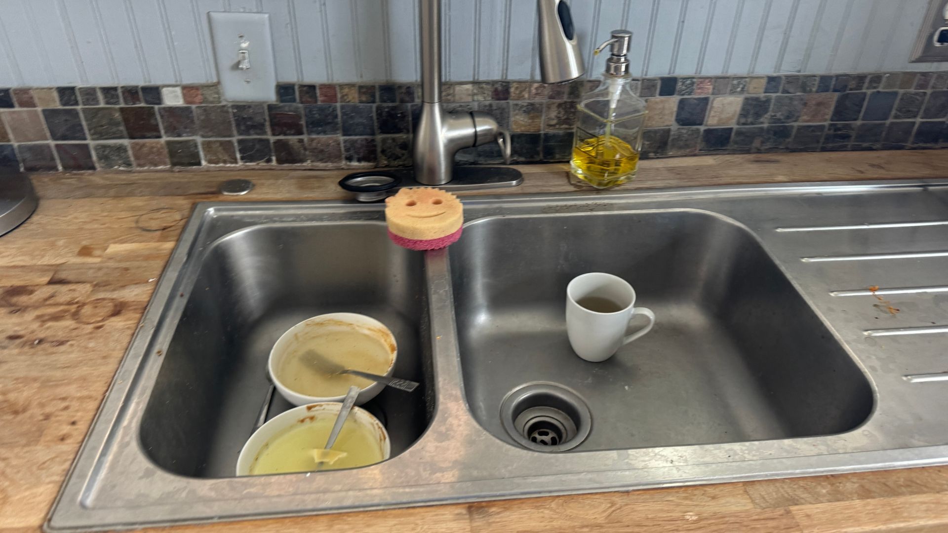 A kitchen sink with two cups and a sponge in it