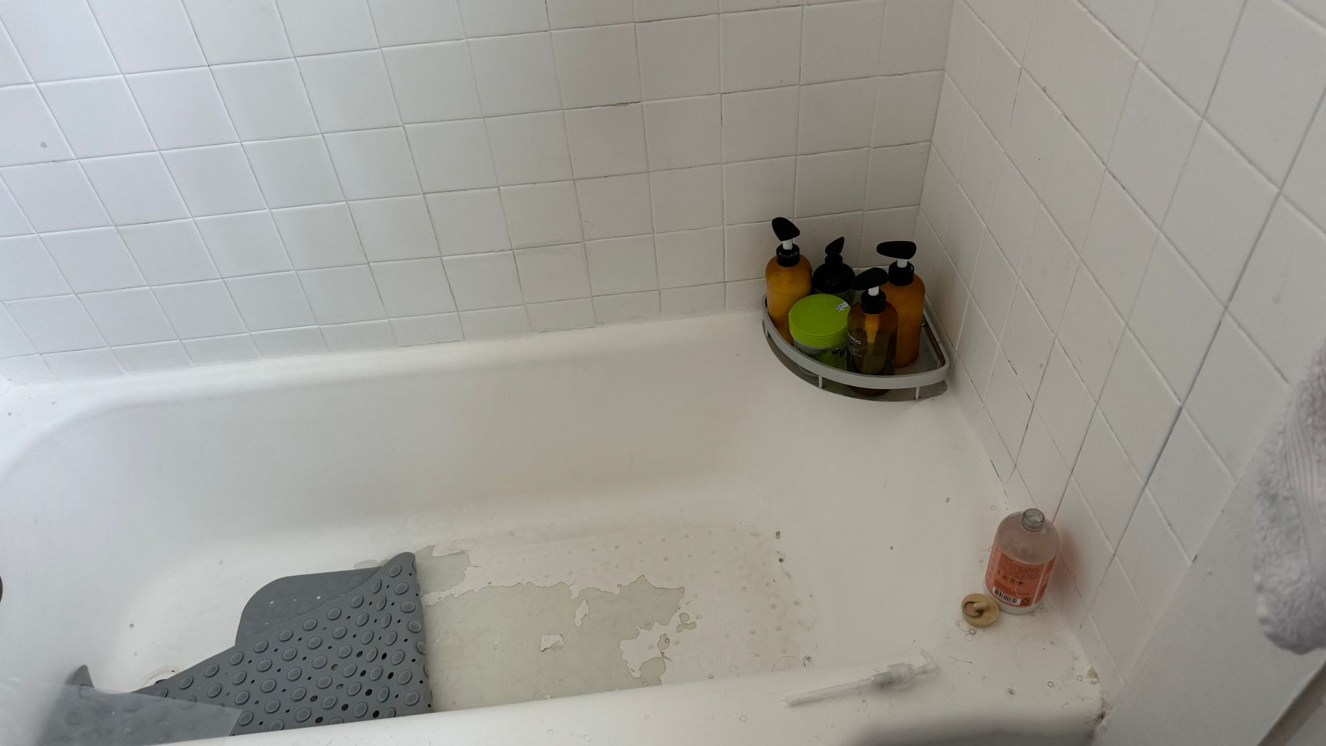 A bathtub in a bathroom with bottles of soap on a shelf.