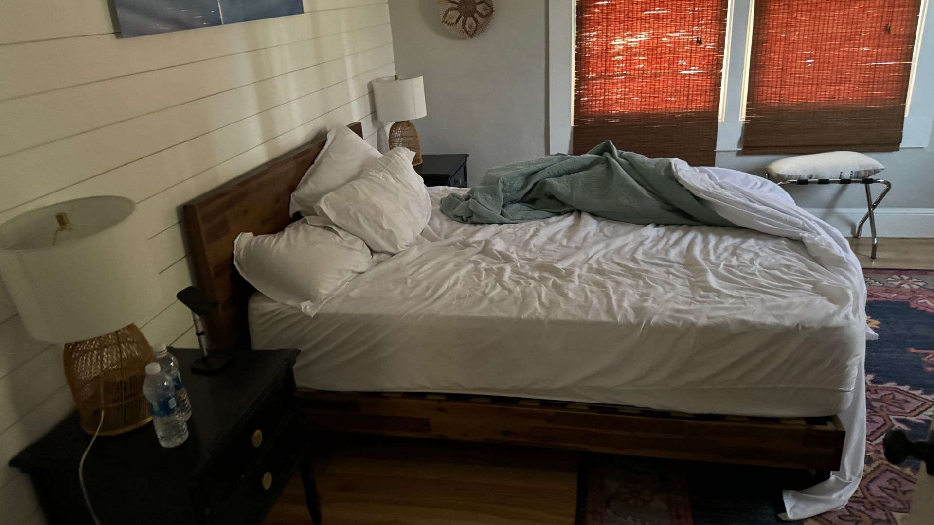 A bedroom with a bed , nightstand , lamp and water bottle.