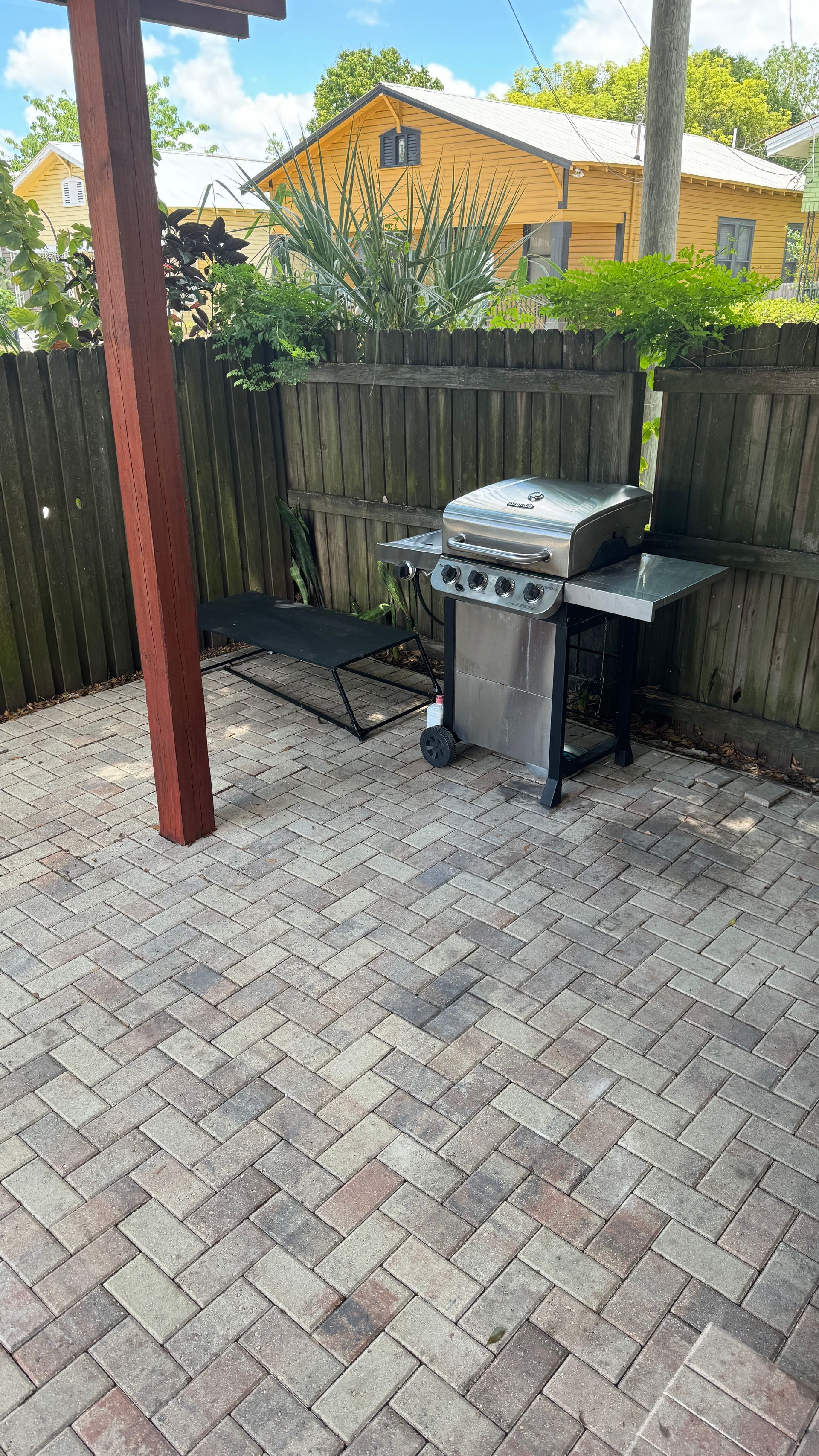 A grill is sitting on a brick patio next to a wooden fence.