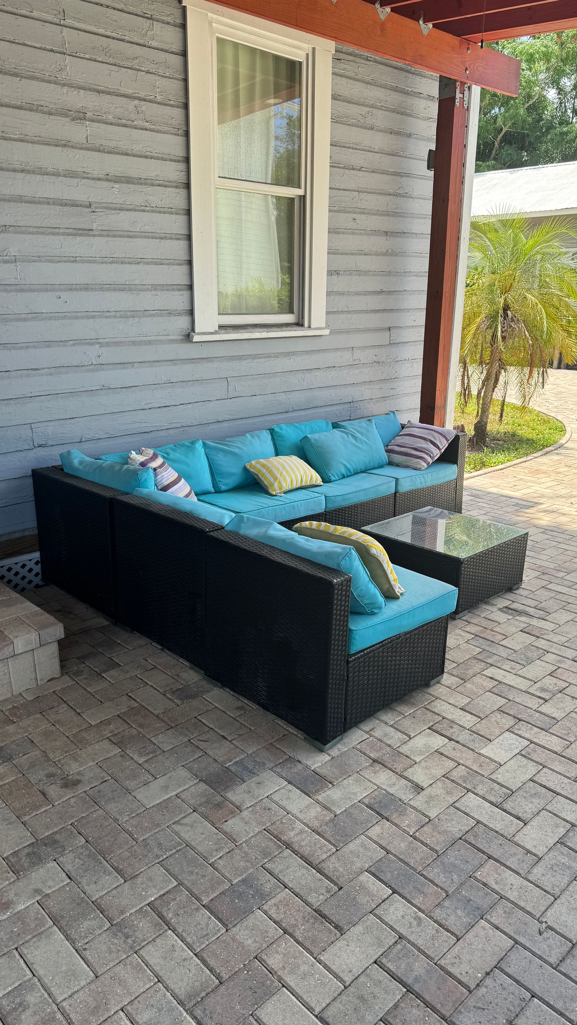 A black sectional couch with blue cushions is sitting on a brick patio in front of a house.