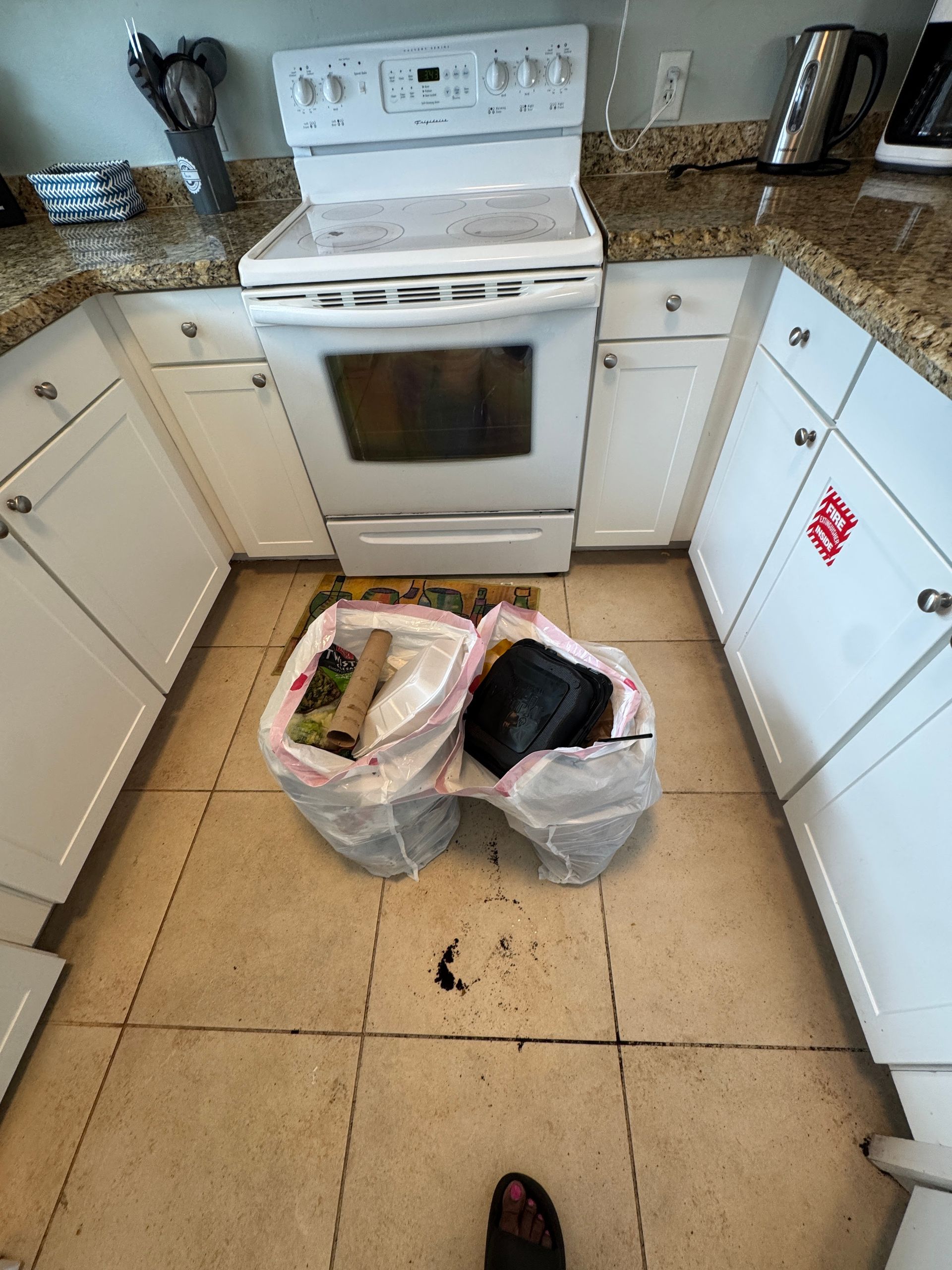 A kitchen with a stove and two trash bags on the floor