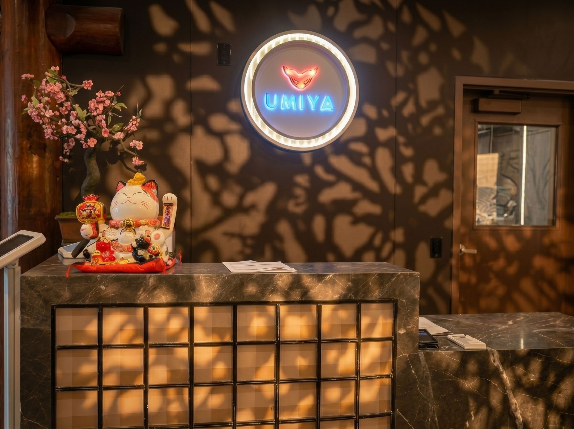 Warmly lit café counter with a glowing circular sign, flowers, and a small decorative statue on the left.