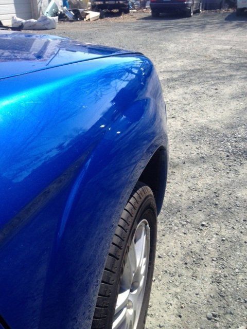 A blue car is parked in a gravel lot