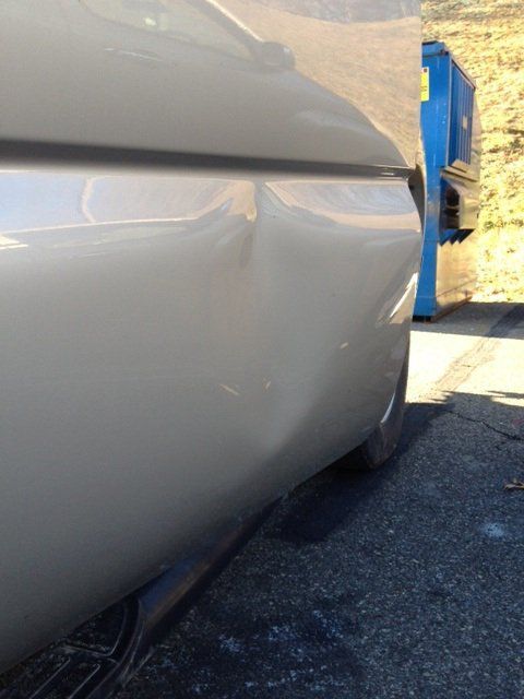 A car with a damaged side is parked next to a blue dumpster