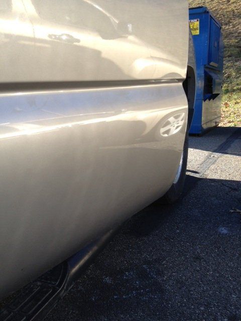 A silver car is parked next to a blue dumpster