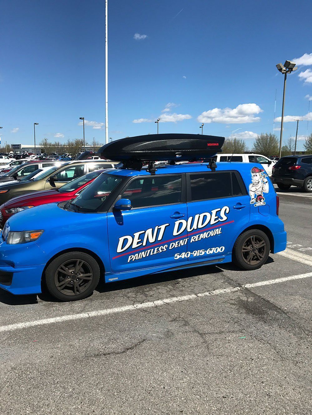 A blue car with a roof rack on top of it is parked in a parking lot.