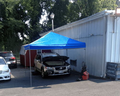 A car is parked under a blue canopy in front of a building