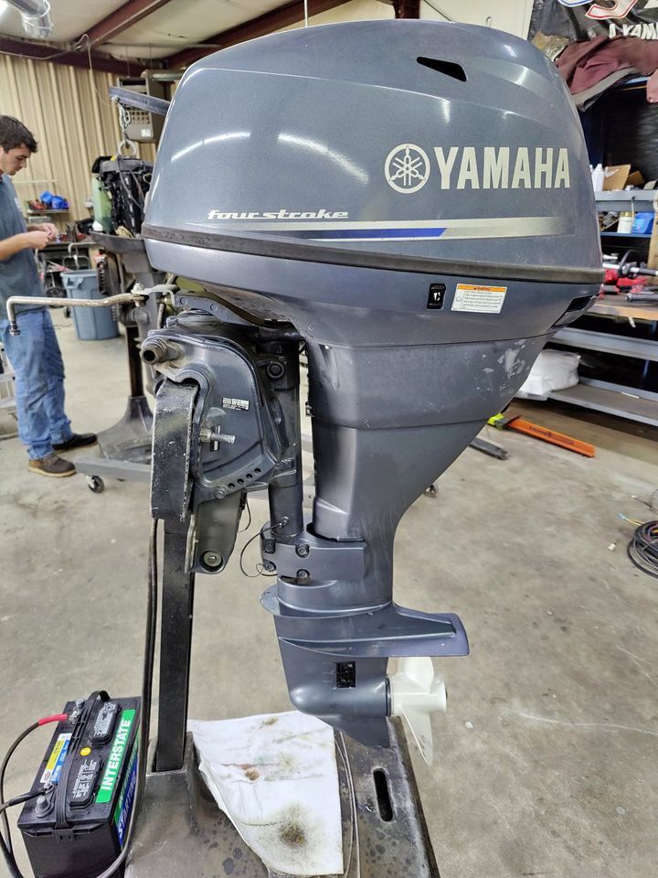 A man is working on a yamaha outboard motor in a garage.