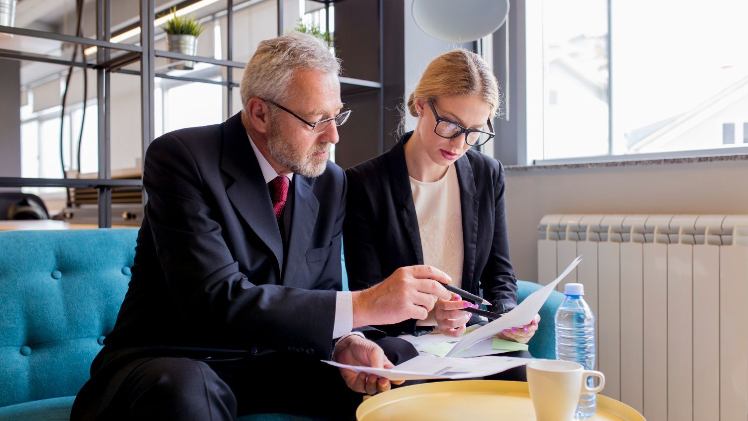 Two professionals reviewing documents on a couch in a bright office