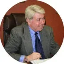 Smiling man in a gray suit and blue tie seated at a desk, facing left
