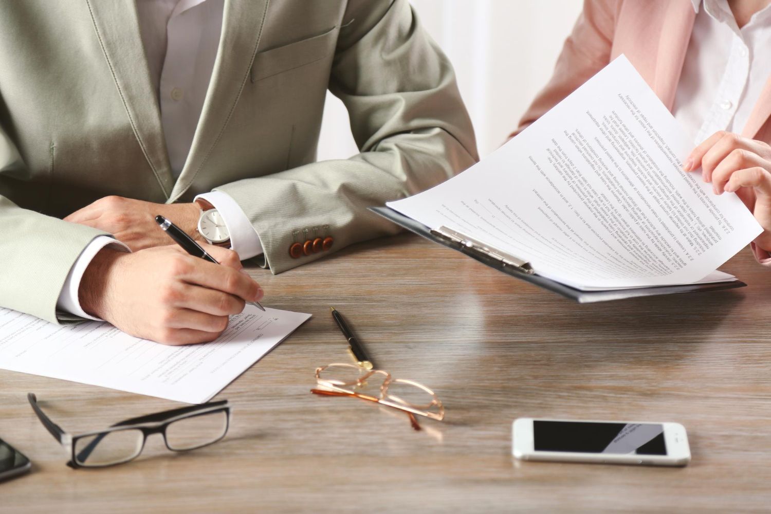 Two people reviewing documents at a wooden table with a pen, glasses, and smartphone