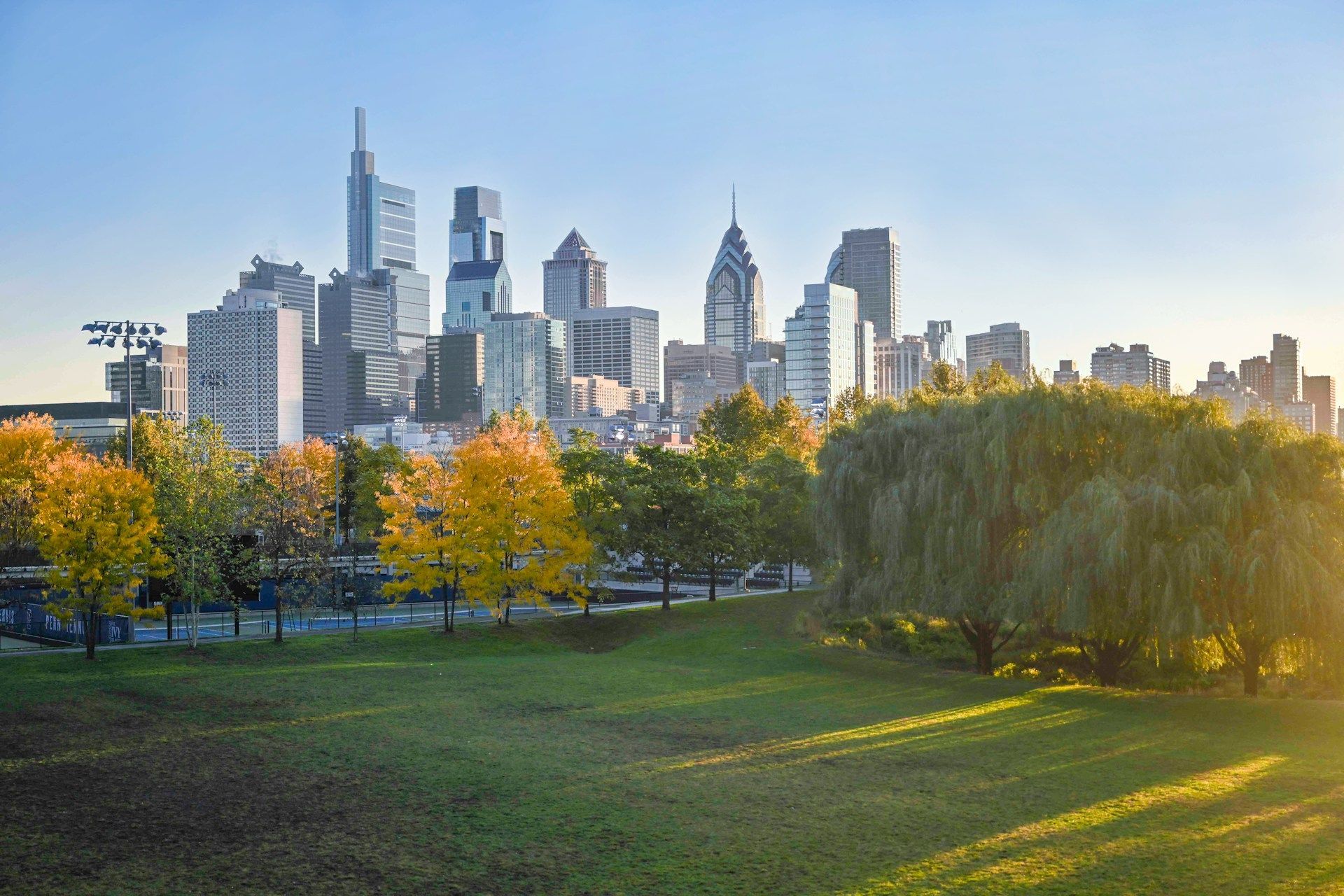 Philadelphia skyline at sunset rising behind a lush, autumn-colored park with green grass in the foreground.