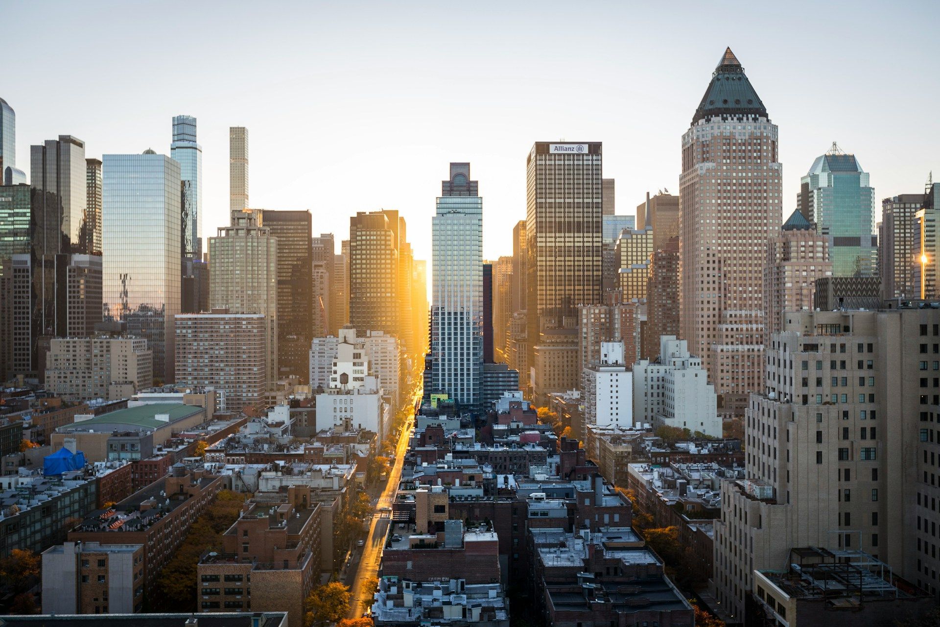 A sunset view of a dense Manhattan cityscape with golden light reflecting off buildings along a street canyon.