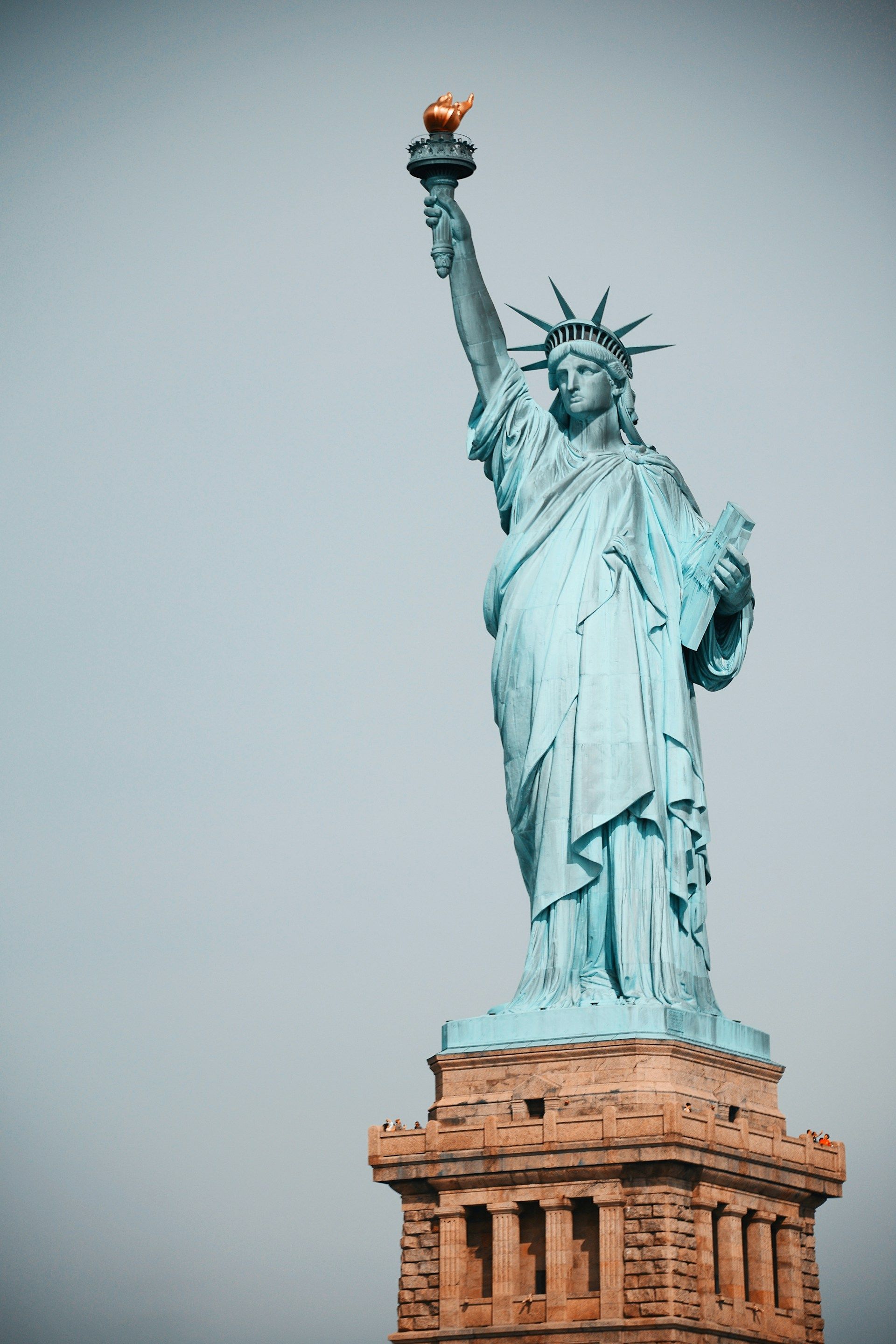 The Statue of Liberty standing atop its pedestal against a plain, light blue sky.