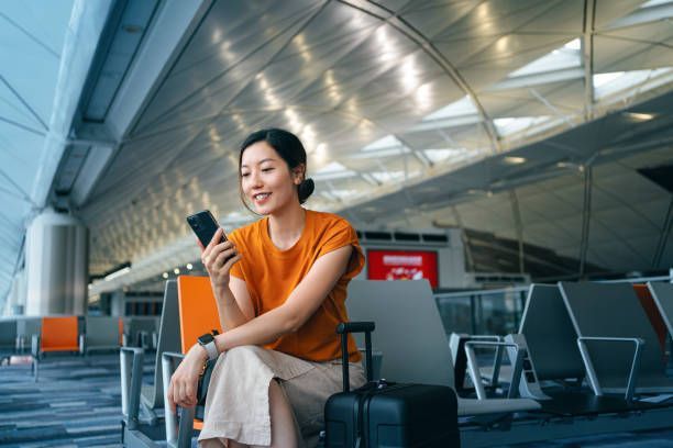 A woman is sitting on a chair at an airport looking at her phone.