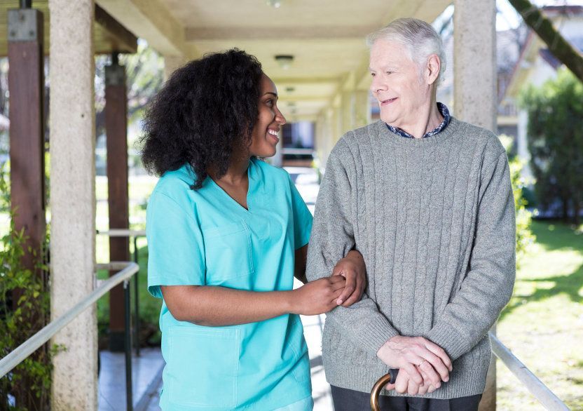 Two people walking together outdoors, smiling and holding arms on a covered walkway.