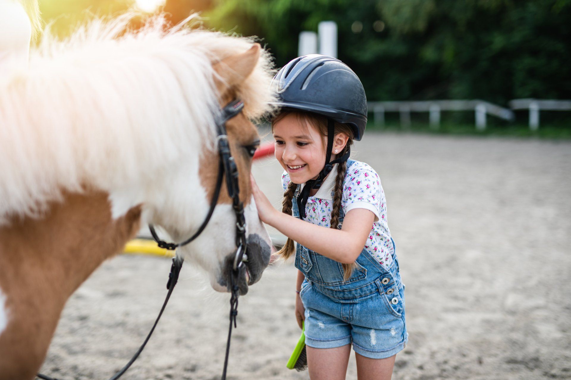 Ein kleines Mädchen mit Helm streichelt ein Pony.