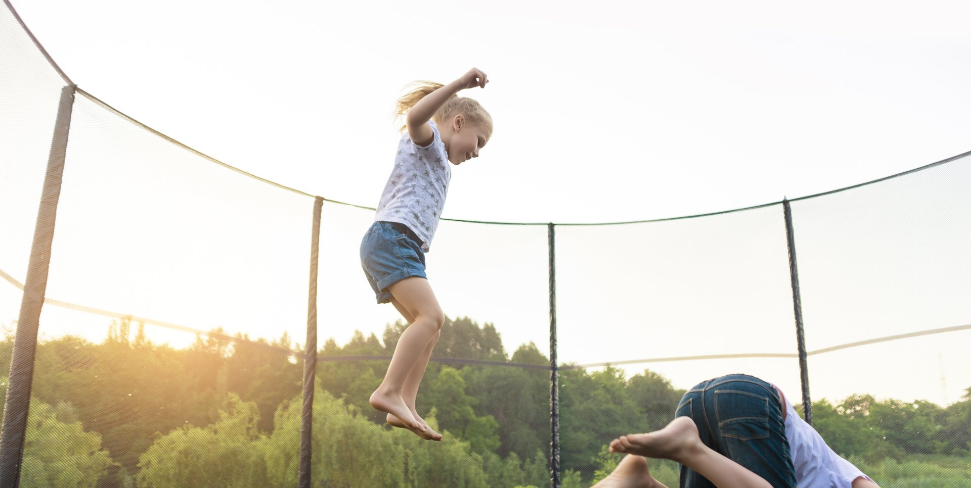 Ein kleines Mädchen springt auf einem Trampolin, während ein Mann zusieht.