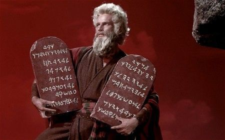 Moses holding the Ten Commandments tablets, standing before a red sky.