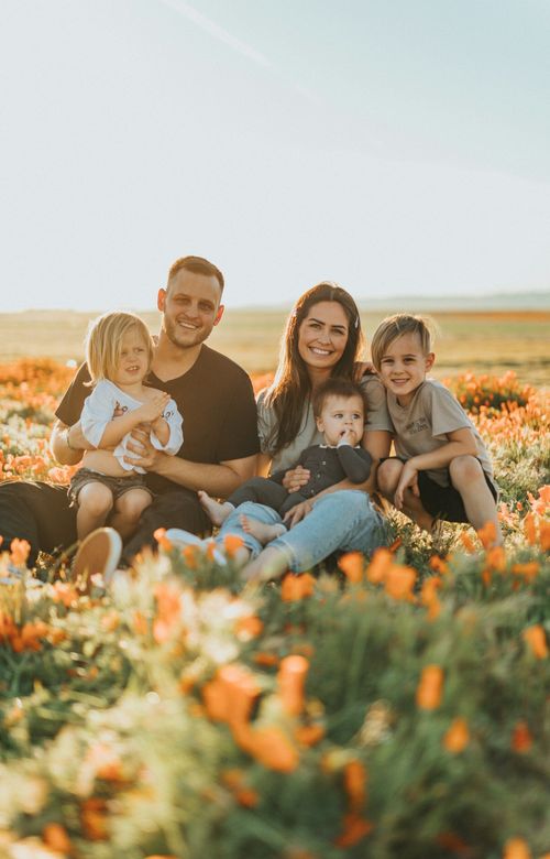 Family sitting together in a flower field at sunset, smiling and holding children