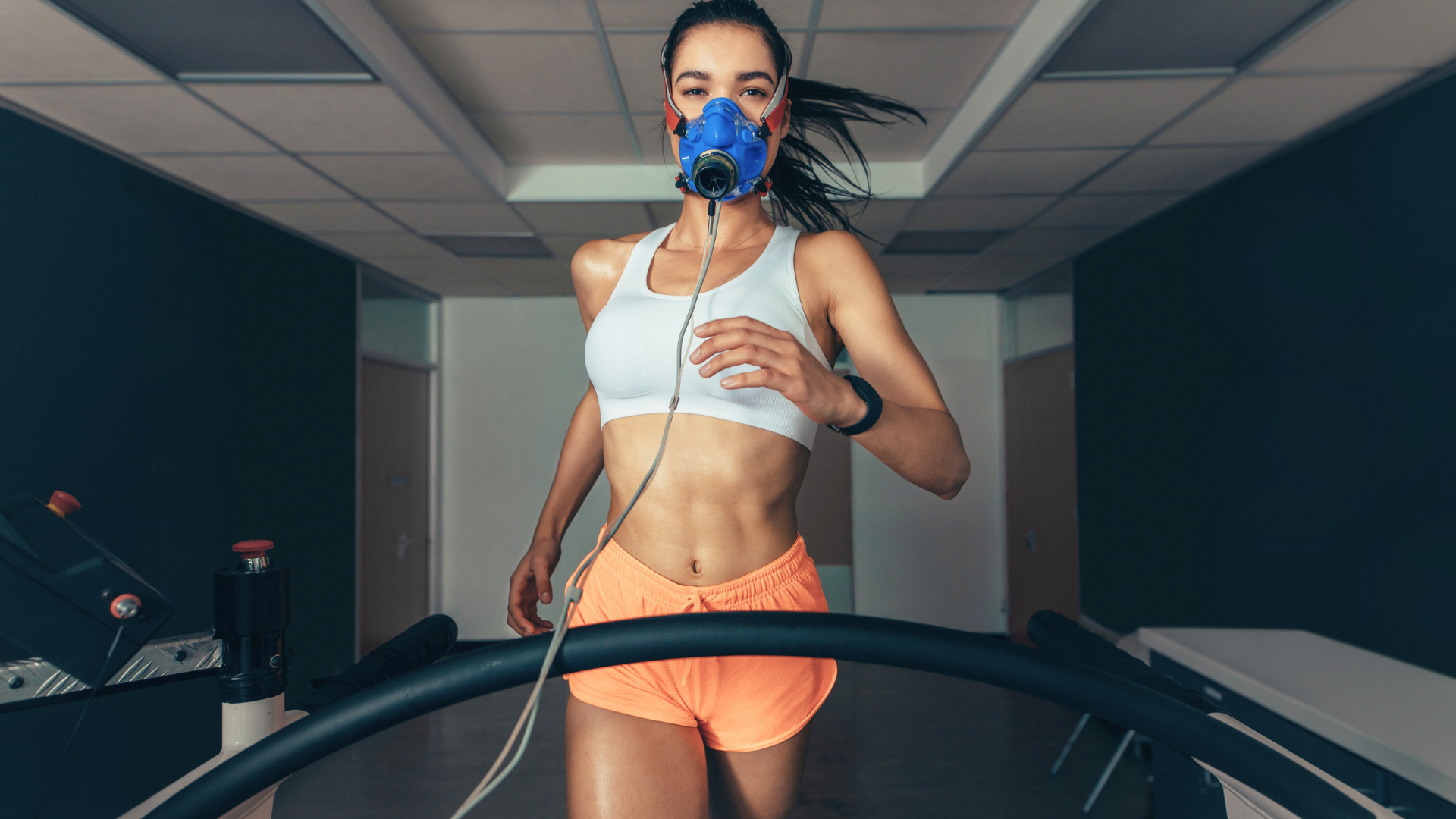 A woman is wearing an oxygen mask while running on a treadmill.