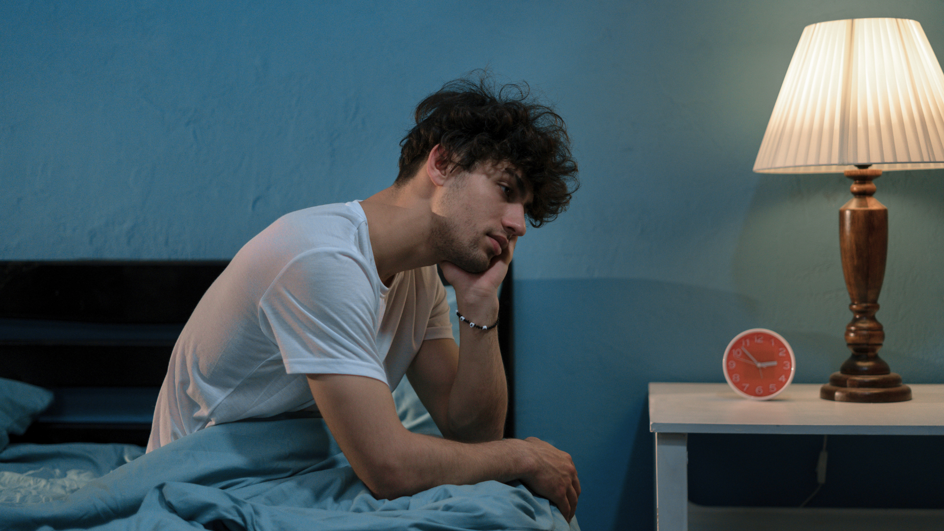A man is sitting on a bed next to a lamp.