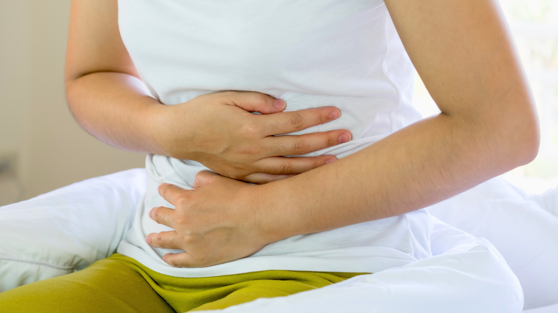 A woman is sitting on a bed holding her stomach in pain.