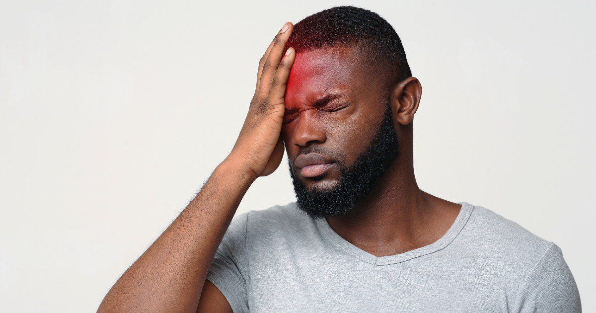 Man with a beard touches his forehead with a pained expression; red glow highlights the area.