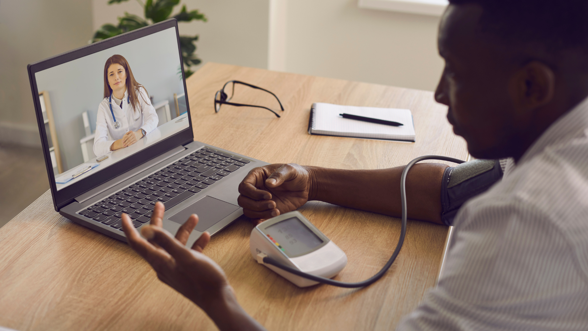 Man taking blood pressure during a telehealth appointment with a doctor on a laptop screen.