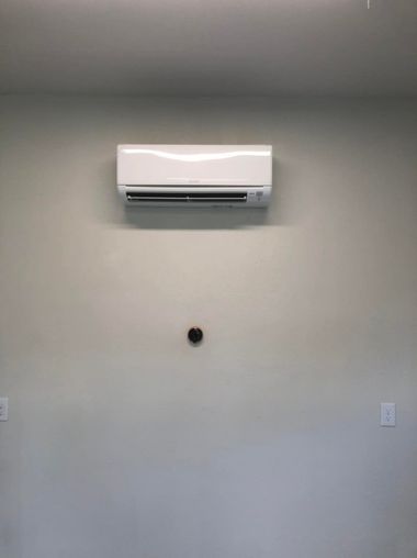 White air conditioner mounted on a light gray wall with a dark brown, circular object below it.