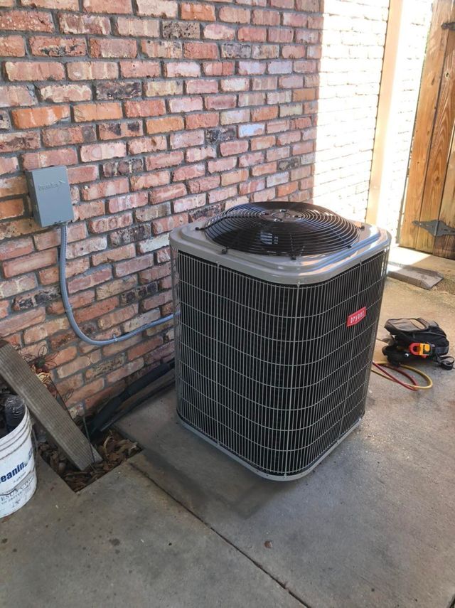 Air conditioning unit against a brick wall. Gray electrical box above, tools on the right, and a concrete slab.
