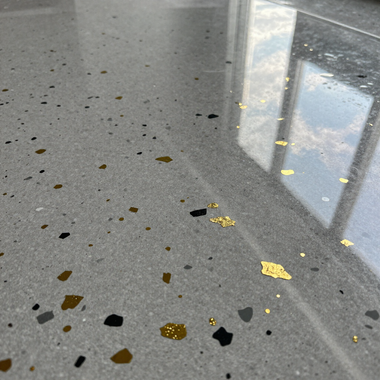 Polished gray terrazzo floor with black, gold, and brown chips reflecting a window