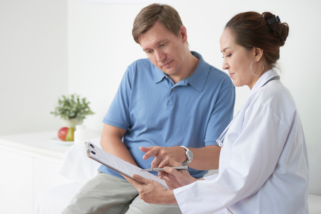 Doctor in white coat reviews paperwork with a patient in a blue shirt, indoors.