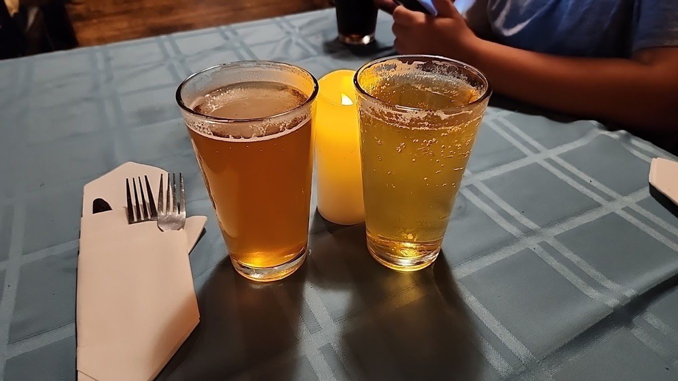 Two glasses of beer are sitting on a table next to a candle.