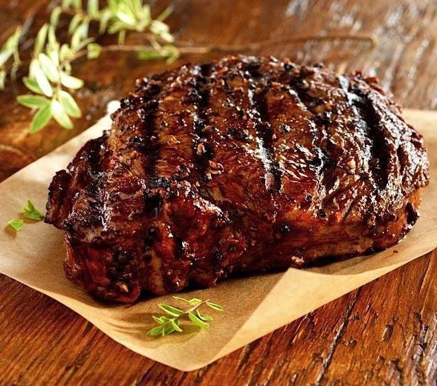 A steak is sitting on a piece of paper on a wooden table