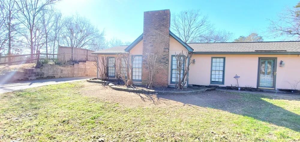 Pink house with brick chimney and bare trees against a blue sky.
