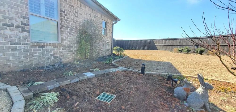 A brick house with a yard and decorative rabbit statues. Brown mulch, gravel, and a wooden fence surround.
