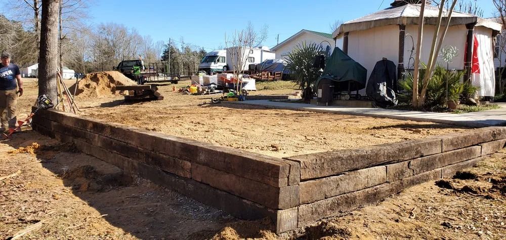 Wooden retaining wall under construction, with dirt and equipment visible in yard.