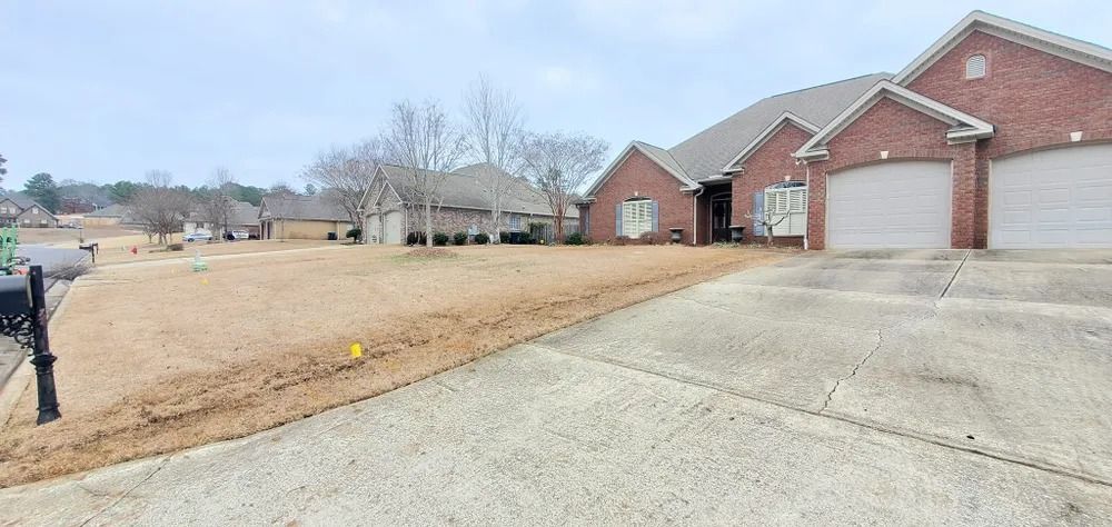 A brick house with a two-car garage on a cloudy day. The lawn is brown and the driveway is gray.