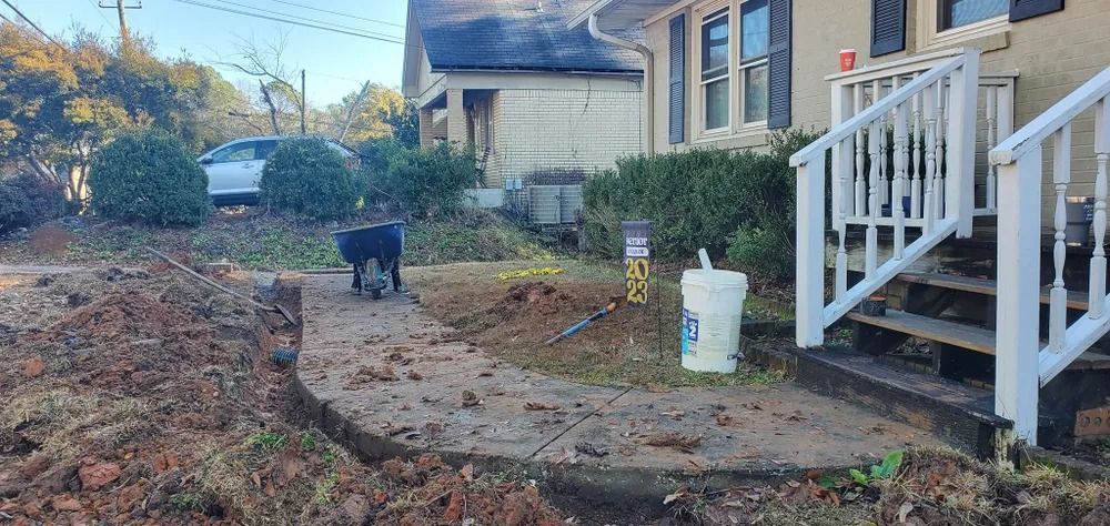 A dog walks on a concrete path, digging. Dirt mounds and trenches around the path lead to a house.
