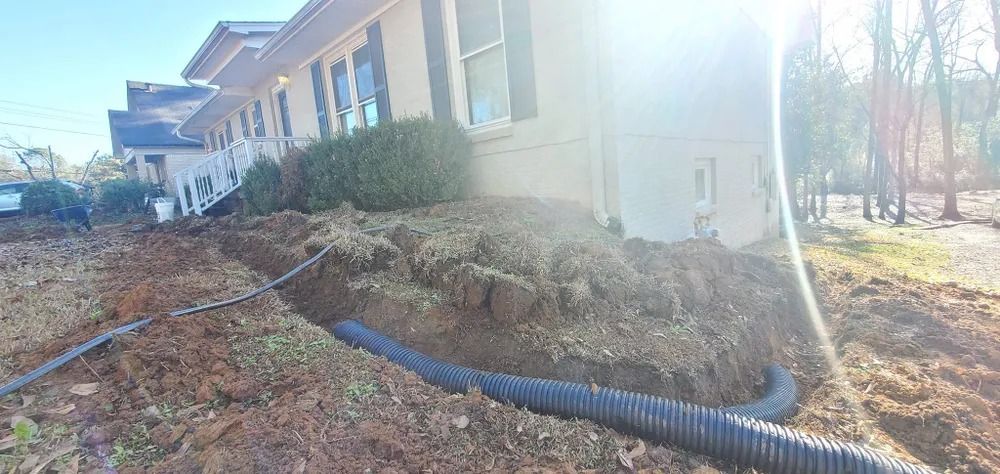 Black corrugated drainage pipe installed near a house, surrounded by dirt.