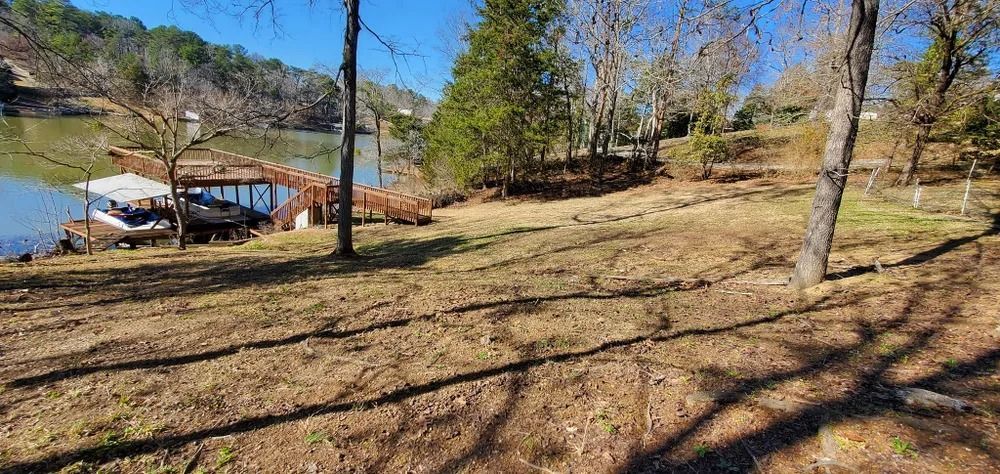 A lakefront property with a dock, boat, and yard; trees, water, and a clear blue sky.