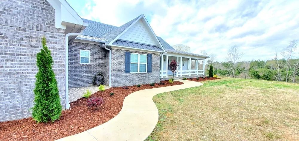 A brick house with a winding walkway, surrounded by landscaping and a grassy yard. Overcast sky.